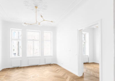 „Jasne, minimalistyczne wnętrze z białymi ścianami, parkietem w jodełkę i wysokimi oknami, które podkreślają elegancję przestrzeni i naturalne światło.”